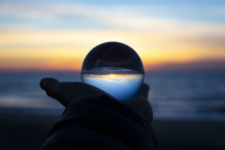 A person handing a glass ball at sunrise.