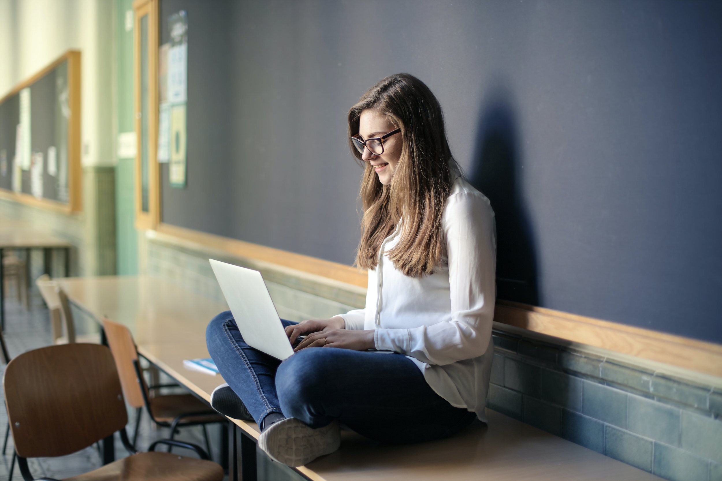 Student sitting on a table against a chalkboard using a laptop.