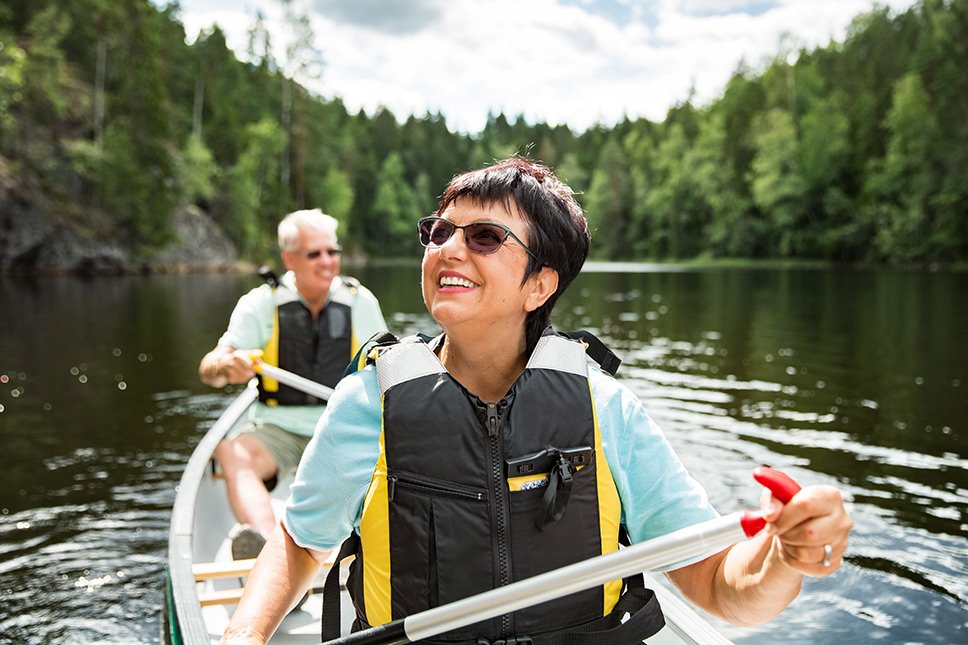 A happy retired couple canoeing on a lake.