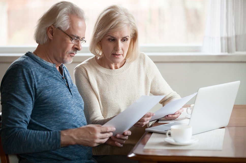 Mature couple looking at their financial statements and using a latop at the table.