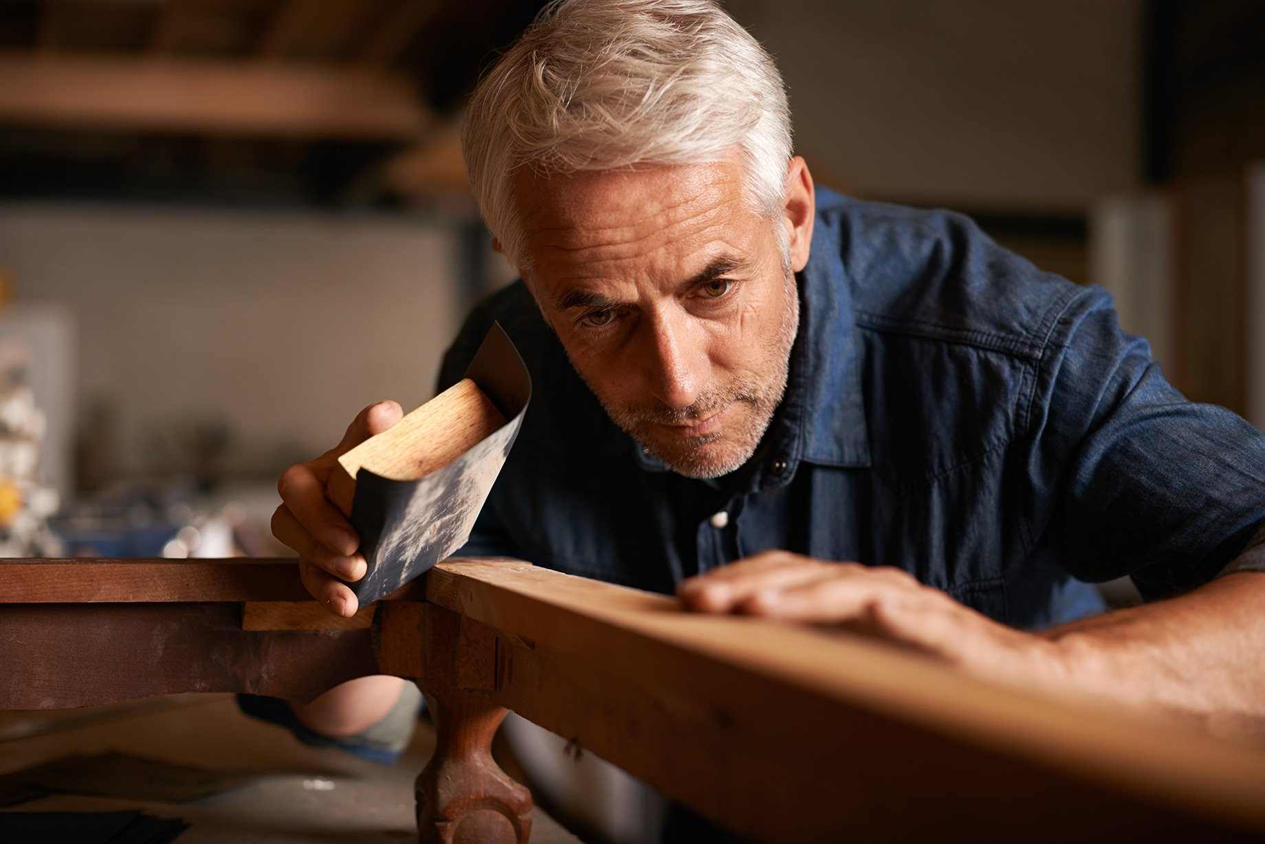 Mature carpenter inspecting his project as he sands it.