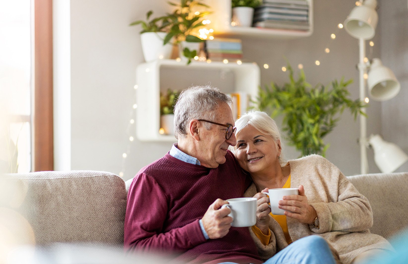 Mature couple snuggling together on the couch holding cups of coffee.