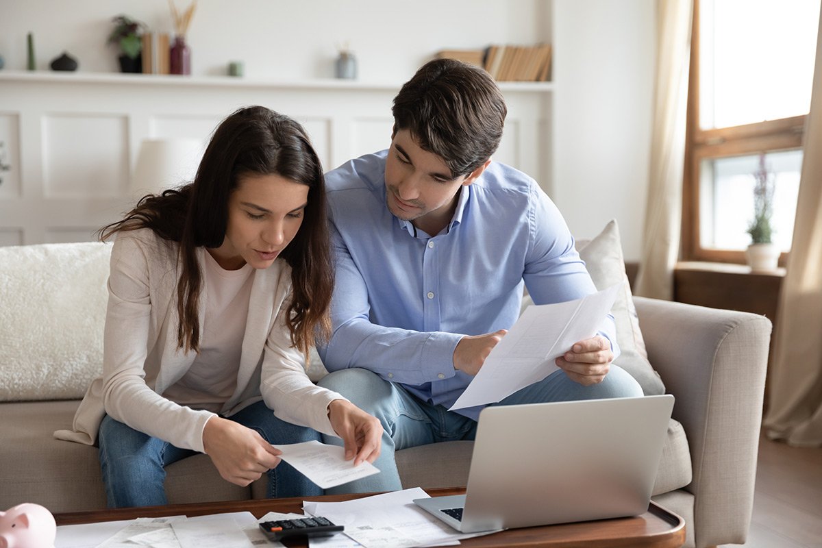 Young couple sitting on a couch totaling their debt using a laptop computer.