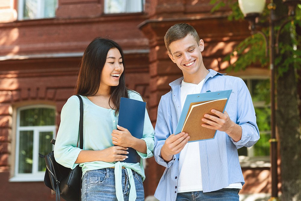 Two college students standing together outdoors smiling on the campus of their college.