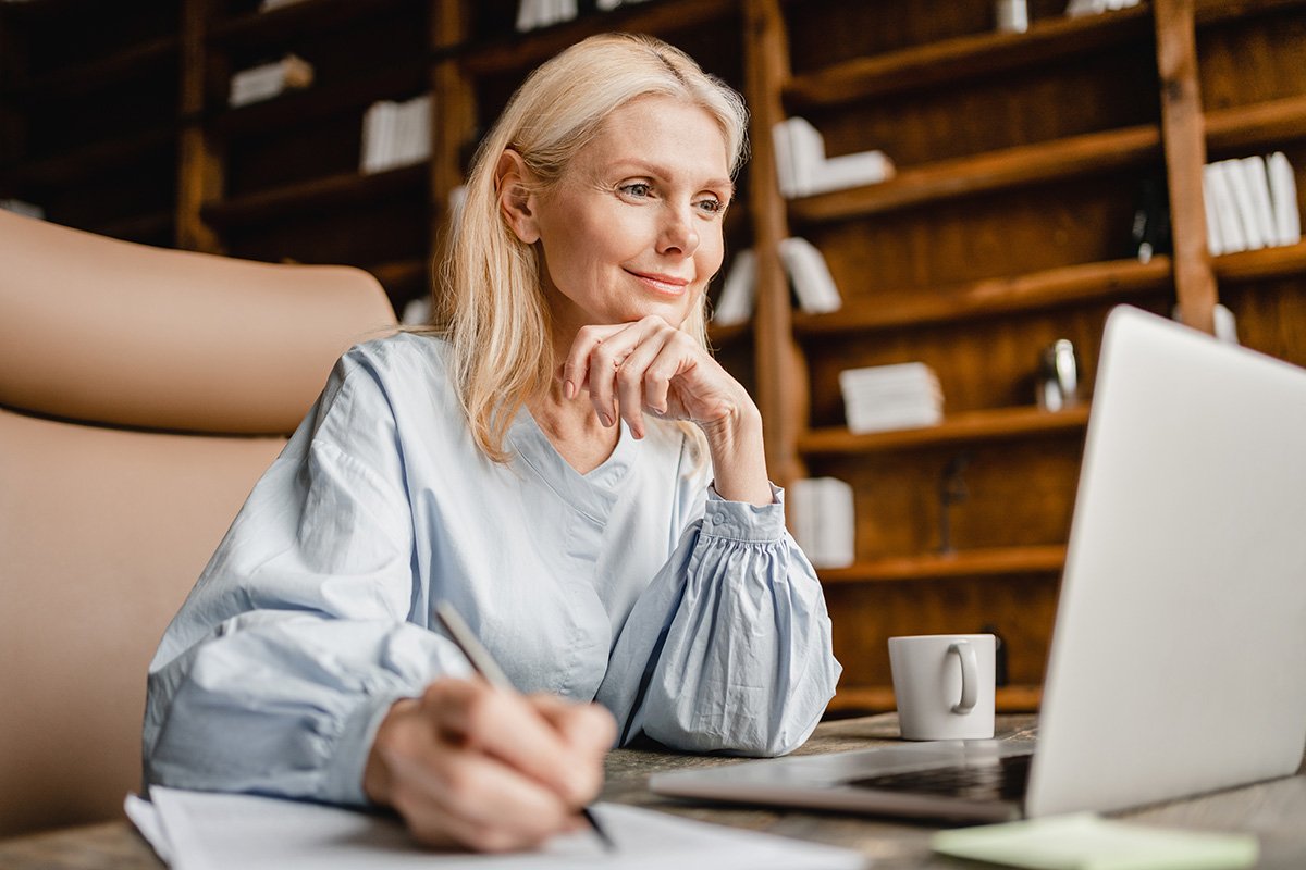 A smiling, confident mature woman sitting at a laptop computer.