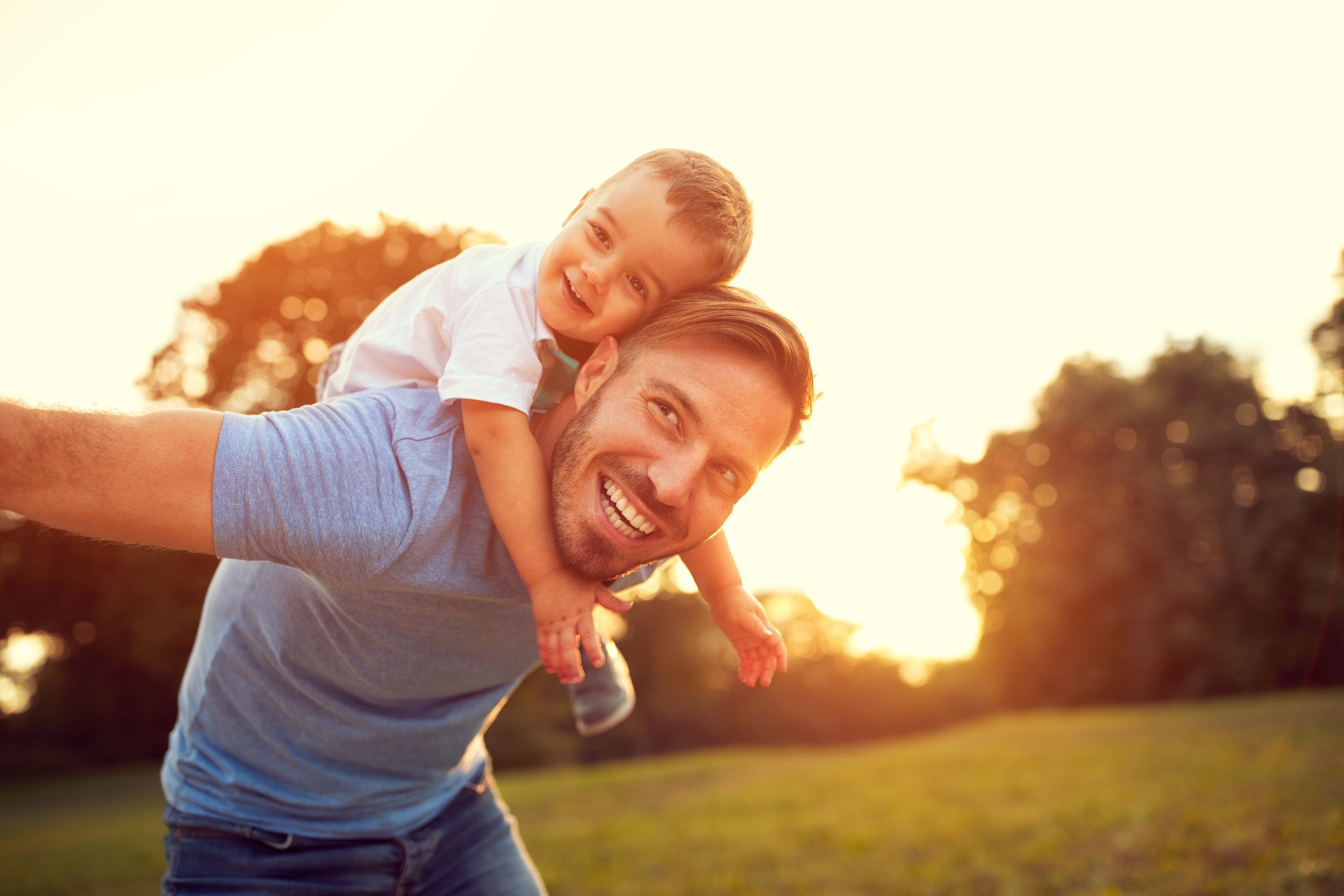 A father carrying his son on his back outdoors at sunset.