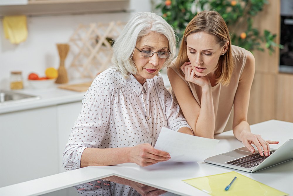 A middle-aged daughter helps her senior mother look over her financial statement.