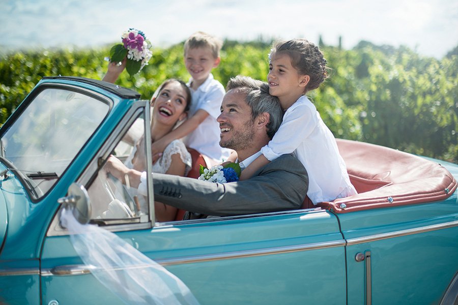 Happy newlyweds with their two children from previous marriages in a convertible car.