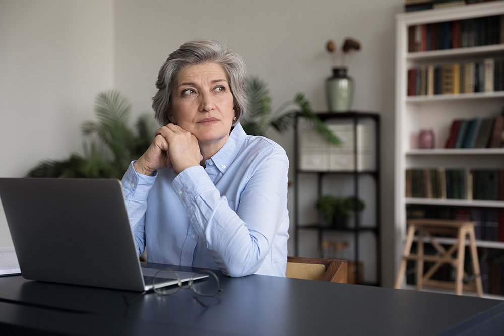 Woman sitting at a laptop staring away thinking about a loved one who passed away.