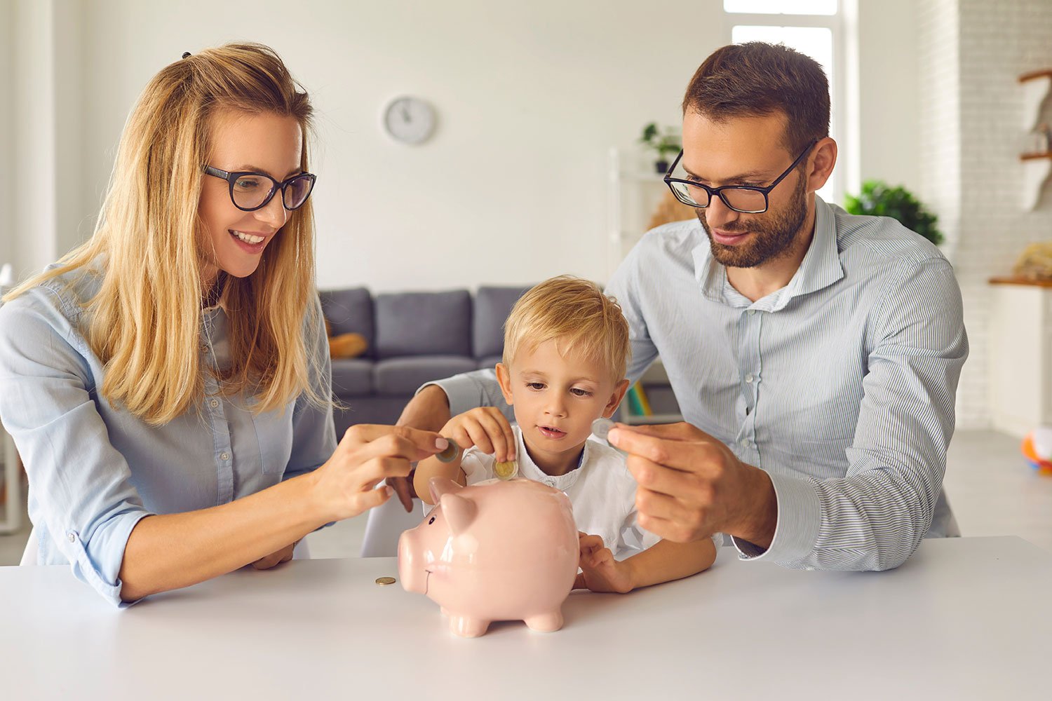 Young parents putting coins in a piggy bank with son.