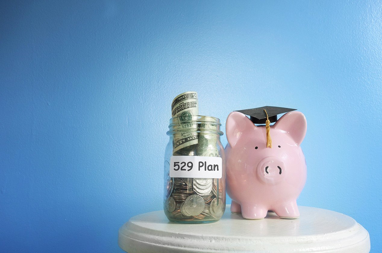 Piggy bank with graduate cap next to a jar of money labeled 529 plan.