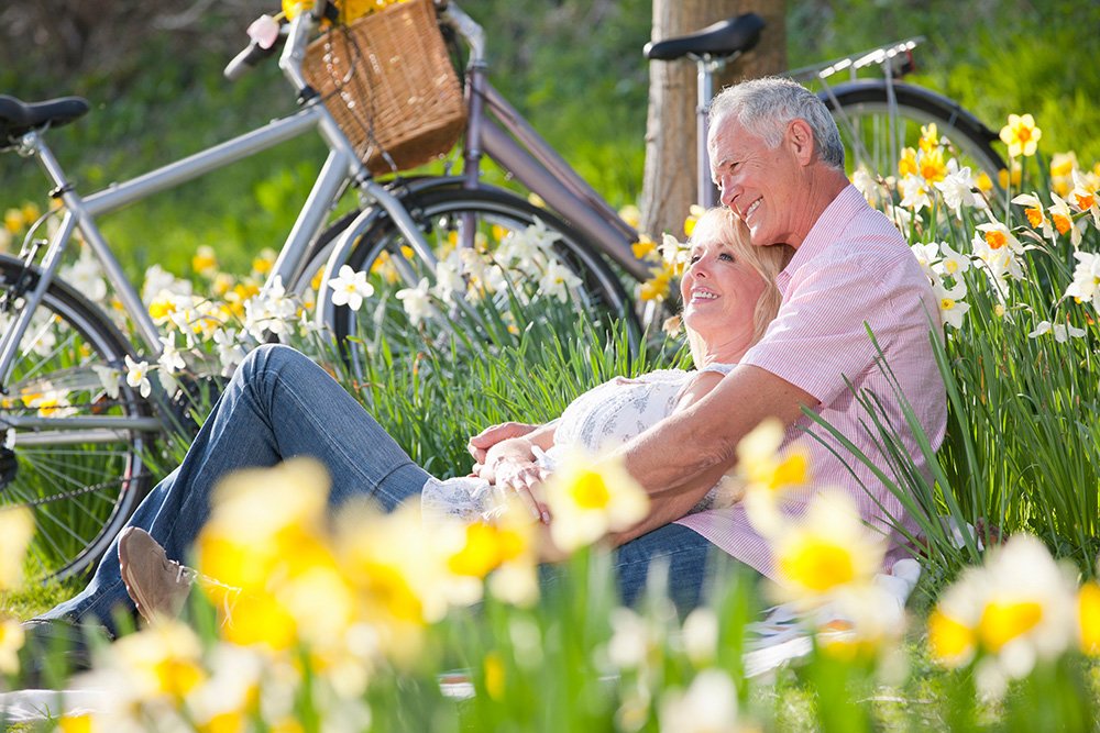 Mature Couple sitting in a field of daffodils with their bikes in the background.