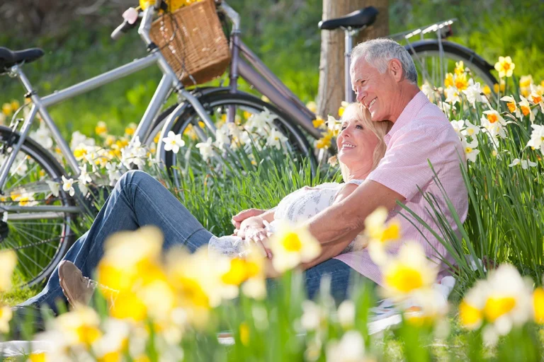 Mature Couple sitting in a field of daffodils with their bikes in the background.