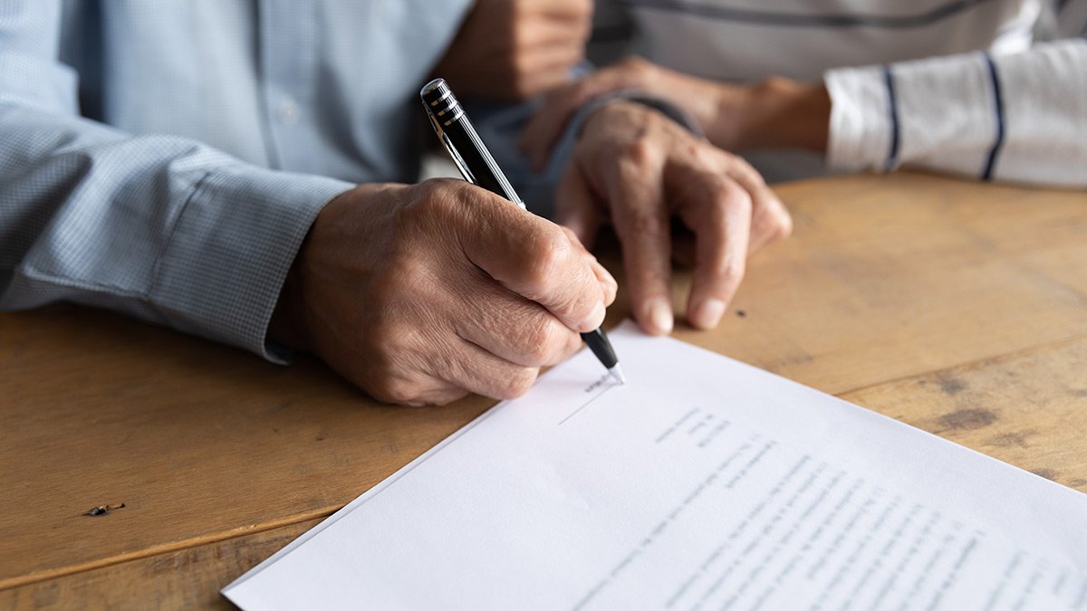 Closeup of Individual signing his name on a document.