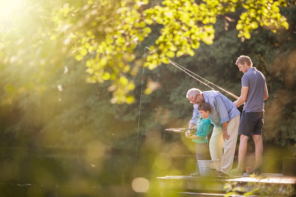 Grandfather, father, and son fishing together on a dock.