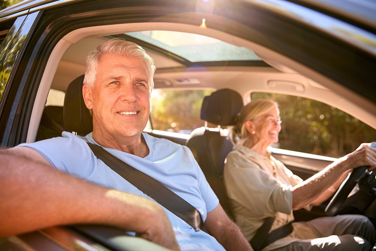 Retired couple driving in a car looking ahead.