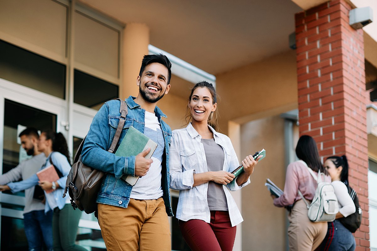 Smiling college students walking out of their school building.