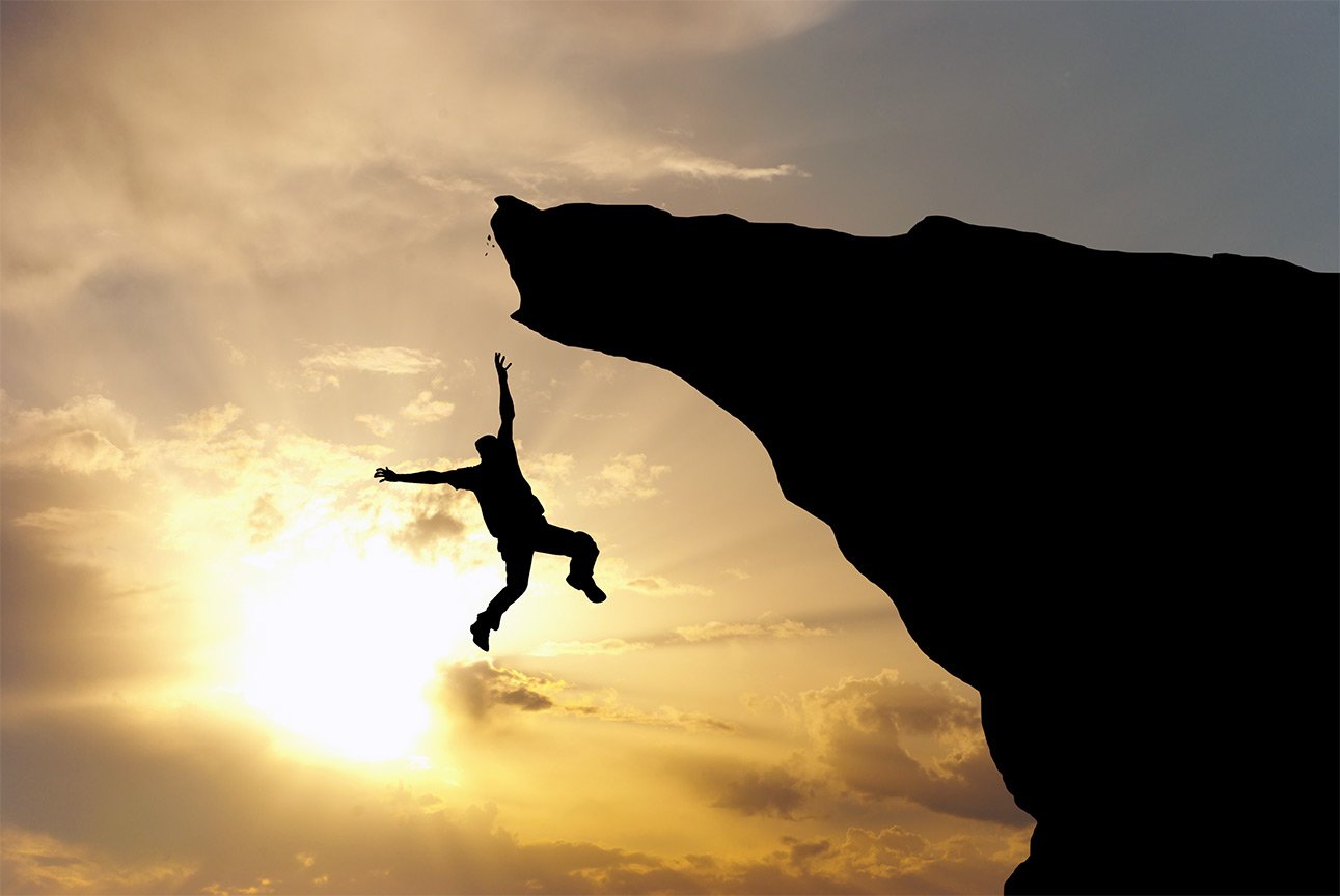 Person falling from cliff silhouetted by sun.