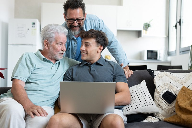 Three generations of men talking on a couch with the youngest holding a laptop.