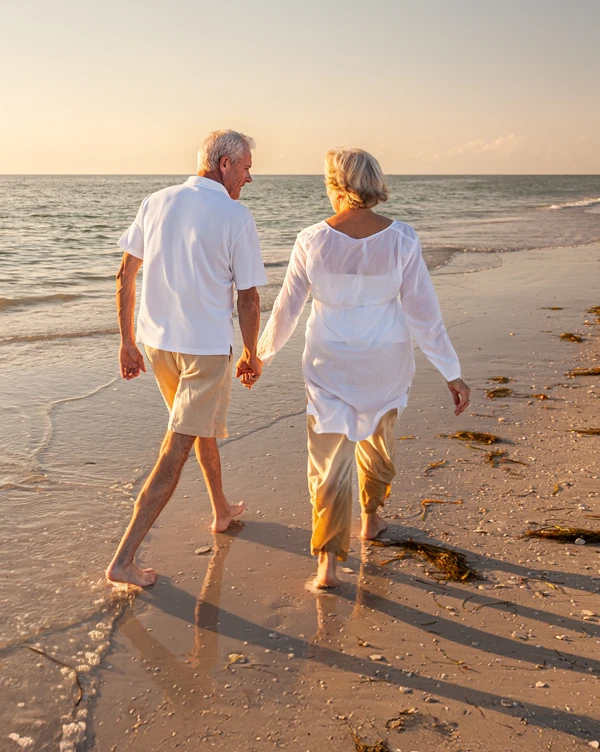 Retired couple walking along the beach, living their best life.