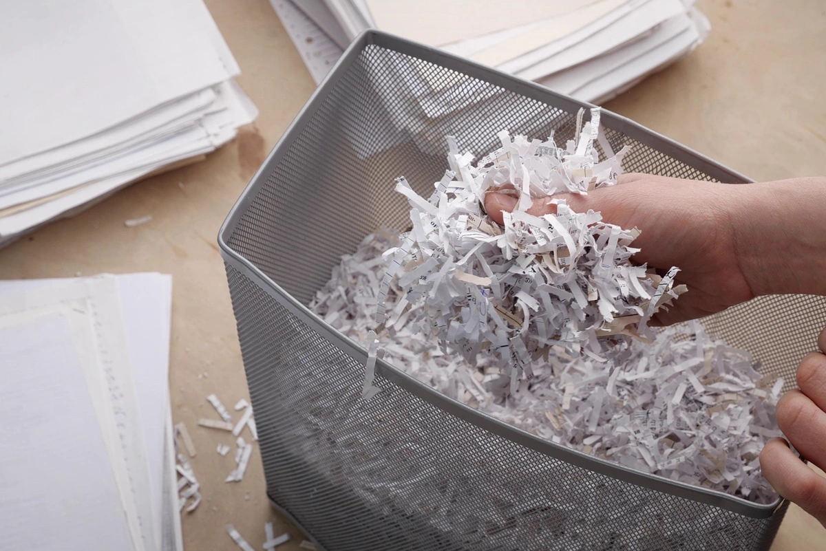 Hands sifting through shredded documents in the bin of a document shredder.