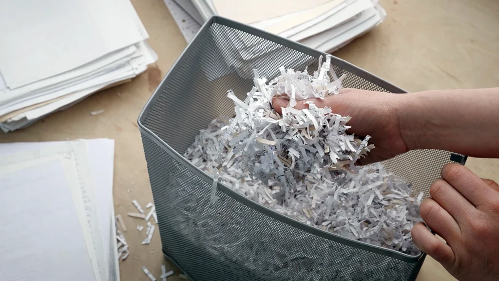 Hands sifting through shredded documents in the bin of a document shredder.