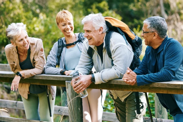 A group of retired friends talking and laughing on a pedestrian bridge while on a hike together.