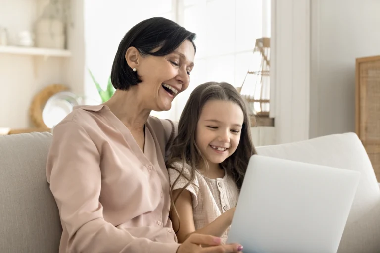 Grandmother sitting with granddaughter on couch using a laptop.