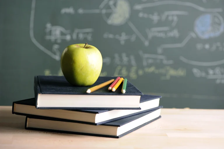 Green apple sitting on books on a desk with chalkboard in the background.