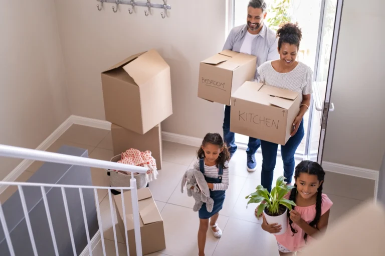 Parents and their two kids walking into their new home carrying boxes.