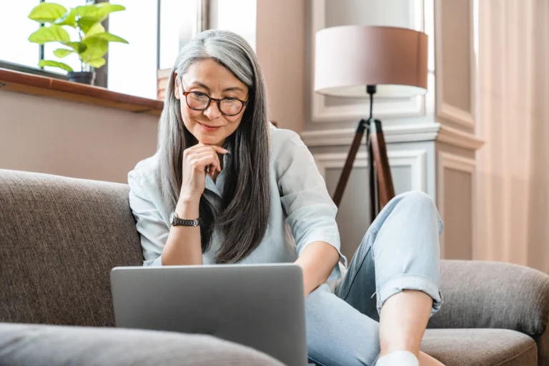 Senior woman sitting on a couch looking at her investments on a laptop.