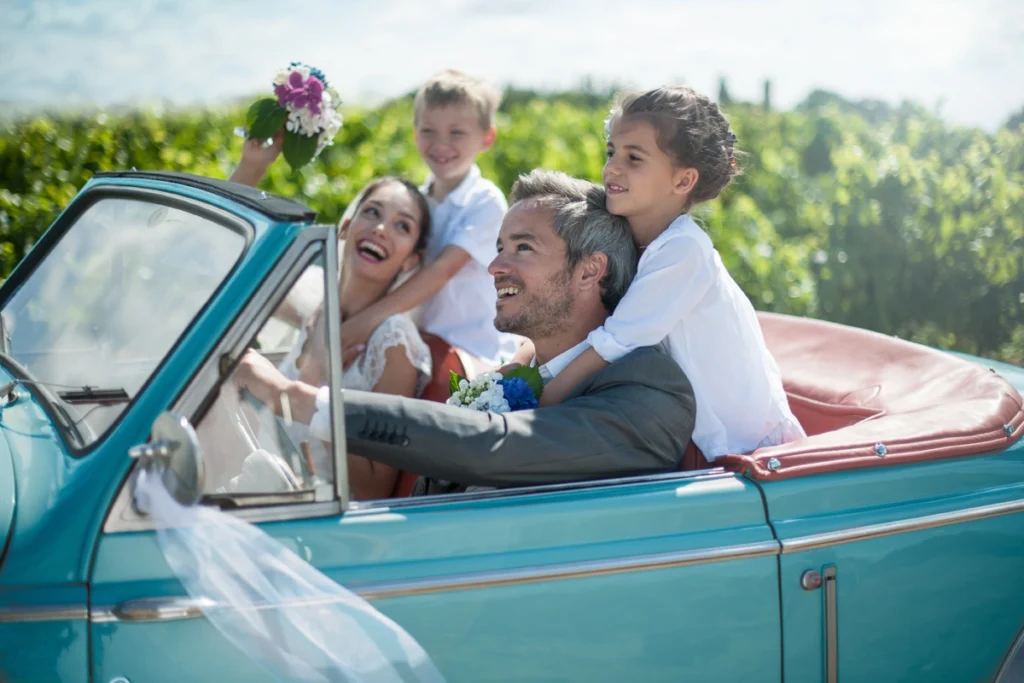Middle-aged newlyweds in convertible with their kids.